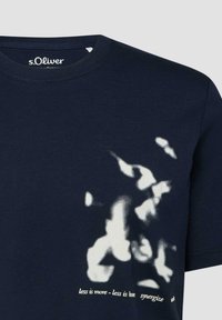 Donkerblauw T-shirt met witte abstracte vormen aan de voorkant en kleine tekst "less is more - less is bon synergize" bij de zoom aan de rechterkant.