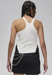 Top a costine bianco con design a schiena scoperta, abbinato a una gonna nera con accenti di catena argentata sui lati.