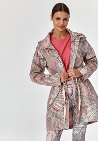 Ružová mikina na zips s kvetinovým vzorom, kapucňou, zúženým pásom a dlhými rukávmi. Nosená over ružovým tričkom a vzorovanými legínami.