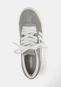 Baskets en suède gris avec lacets et accents blancs. Elles possèdent une semelle intérieure texturée et un logo de marque au bas. Design sportif classique.