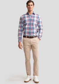 Heren geruite overhemd in blauw, rood en wit, gecombineerd met beige chino's en witte sneakers. Het overhemd heeft een klassieke kraag en een knoopsluiting.