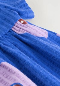 Nahaufnahme von weichem blauen und lila geripptem Stoff mit cartoonartigen Augenmuster auf einem hellen Hintergrund.