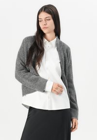 Gray knit cardigan with ribbed cuffs, open front, and soft texture, worn over a white collared shirt and black skirt.
