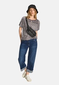 Sort mønstrede top med korte ærmer, blå cropped jeans med opfoldede måneder, hvide sneakers og en sort crossbody taske. Sort bøttehat.
