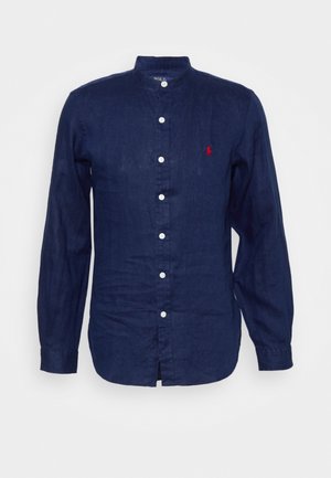 Camicia in lino blu navy a maniche lunghe con colletto alla mandarina, bottoni bianchi sulla parte anteriore e piccolo logo rosso ricamato sul lato sinistro del petto.