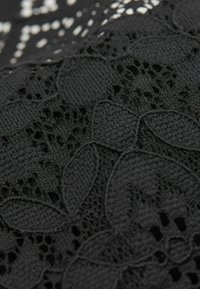 Schwarzer Stoff mit aufwendigen Spitzenmustern neben strukturiertem Gewebe, das eine Mischung aus glatten und offenen Webarten zeigt.