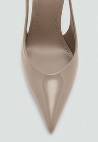 Nude high-heeled shoe with a pointed toe, smooth patent finish, open sides, and a sleek silhouette. Minimal stitching detail visible.