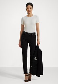 Vit kortärmad åtsittande skjorta, svarta slim-fit jeans med bälte, svart jacka i ena handen och svarta remsandaler med hög klack.