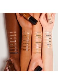 Three arms displaying swatches of foundation shades in various tones from deep to light, with product bottles partially visible.
