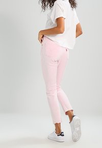 Vaqueros de mezclilla rosa con un largo de tobillo recortado, dobladillo deshilachado y bolsillos traseros. Combinados con una camiseta blanca y zapatillas deportivas blancas.