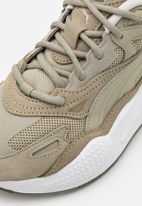 Beżowe sneakersy z połączeniem zamszu i materiału siatkowego, z teksturowanymi akcentami, wyściółką języka oraz białą, teksturowaną gumową podeszwą.