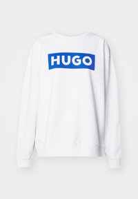 Felpa bianca con collo rotondo e maniche lunghe. Presenta una grafica rettangolare blu con il testo "HUGO" in bold di colore bianco.