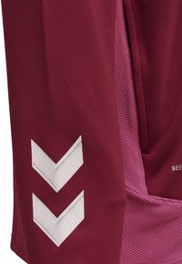 Maroonsportbukser med tekstureret pink sidepanel, der har et hvidt chevronmønster på venstre ben; lavet af åndbart stof.