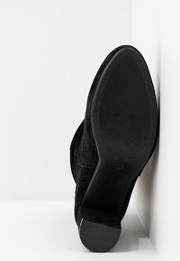 Black suede ankle boot with a textured sole, block heel, and rounded toe. Upper features a smooth finish and hidden stitching detail.