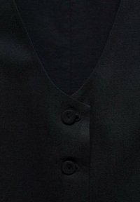 Svart tygblus med V-ringning, två knappar och en slät textur med en subtil lyster. Enkel och minimalistisk stil.