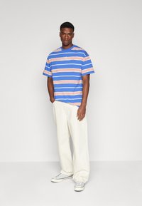 Camiseta de rayas azules con rayas naranjas y blancas, cuello redondo, mangas cortas, corte casual, combinada con pantalones de pierna ancha en color crema y zapatillas ligeras.