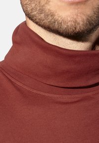 Bordeauxfarbener Rollkragenpullover mit enganliegender Passform. Texturiertes, dehnbares Material mit umgeschlagenem Kragen. Nahaufnahme, die die Nähdetails hervorhebt.