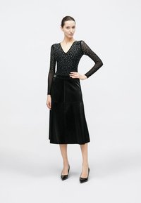 Μαύρο κορμάκι με μακριά, διάφανα μανίκια και λαμπερά κρύσταλλα, συνδυασμένο με μαύρη δερμάτινη midi φούστα και μαύρες μυτερές γόβες.