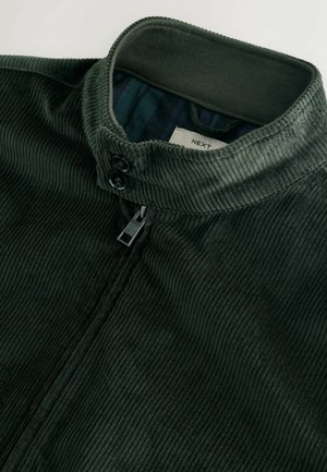 Donkergroene corduroy jas met een hoge kraag, twee knopen en een ritssluiting. De binnenkant heeft een contrasterende geruite voering.