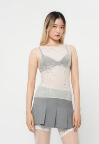 Top grigio trasparente con ricami floreali e paillettes, indossato su una gonna a pieghe grigia chiara, completato da pantaloncini bianchi con pizzo.