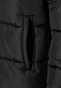 Sección de chaqueta acolchada negra con un bolsillo con cremallera, textura acolchada, exterior de nylon brillante y áreas fruncidas para aislamiento.