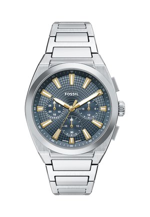 Montre en acier inoxydable argentée avec un cadran texturé bleu, des accents dorés et des sous-cadrans chronographes. Comprend des index lumineux et un bracelet poli.