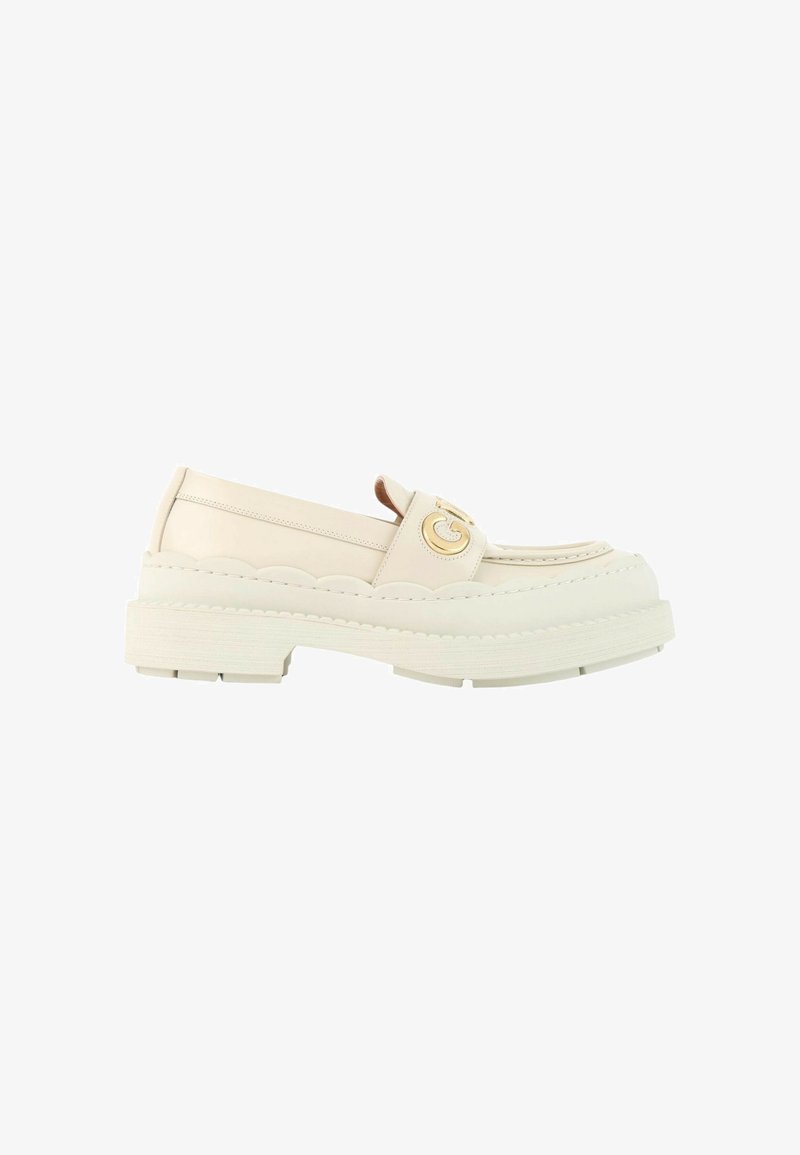 Mocassin en cuir blanc cassé avec semelle épaisse, détails en bords festonnés et boucle décorative dorée sur la bride supérieure.