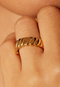 Gouden ring met een gedraaide ontwerp, met gladde, gepolijste oppervlakken en een ronde vorm, gedragen op een vinger tegen een neutrale achtergrond.
