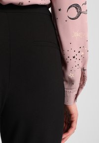 Svarta tygbyxor med sidoficka, tillsammans med en rosa blus som har gyllene och svarta himmelmönster av stjärnor och månar.