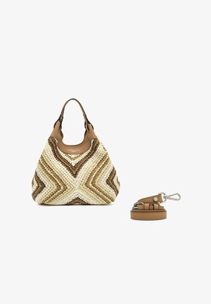 Bolso tejido beige y marrón con asas de cuero y correa de cuero marrón desmontable con cierre plateado sobre fondo blanco.