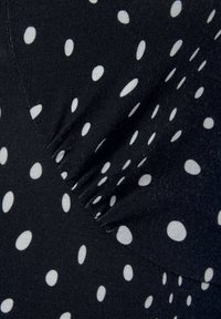 Czarna tkanina z białymi kropkami, z marszczonym wykończeniem przy szwie dla dodatkowego detalu. Gładki i lekki materiał.