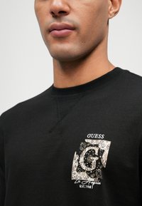 Sweatshirt preto com um logótipo 'G' padrão e detalhes em dourado. Gola canelada e costuras nos ombros, tecido texturizado.