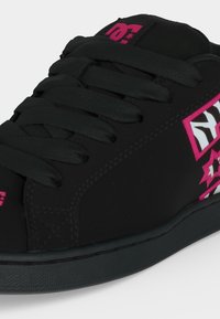 Baskets noires avec des lacets épais, présentant des détails abstraits d’étoile et de logo rose et blanc sur le côté et la languette.