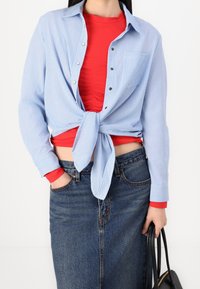 Blue and white striped button-up shirt tied at the waist over a red fitted top, paired with high-waisted denim skirt and black handbag.