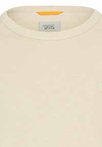 Beige ronde hals t-shirt, gemaakt van zachte stof. Heeft een oranje accent bij de halslijn en een klein logo patch op de borst.