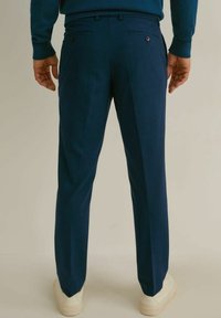 Pantalon formel bleu marine à coupe droite, deux poches arrière avec boutons, et texture lisse, associé à des baskets blanches.