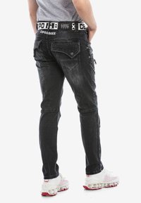 Zwarte denim jeans met gestanste accenten op de achterzakken en een gewatteerde textuur aan de zijkanten; heeft een contrasterende merkband.