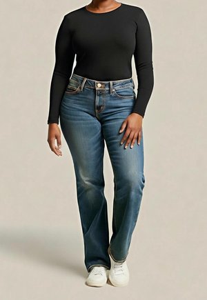 Person, die ein eng anliegendes schwarzes Langarmshirt, blaue Jeans mit geradem Bein und weiße Turnschuhe vor einem schlichten Hintergrund trägt.