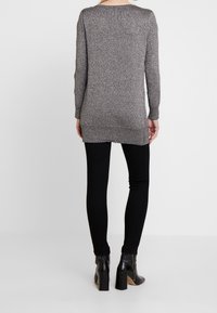 Long-sleeve, gray shimmer tunic with a round neckline, side slits, worn over black skinny pants and heeled ankle boots.