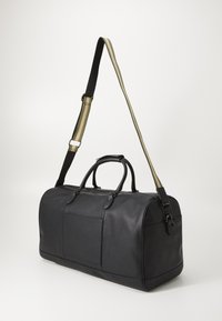 Black leather duffle bag with double handles, a detachable striped shoulder strap, and a front pocket. Textured surface and rounded shape.