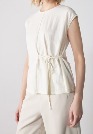 Haut à manches courtes de couleur crème avec une coupe décontractée, comprenant une taille cintrée et un subtil détail de lien. Tissu doux et léger avec une texture lisse.