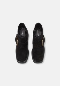 Bottines en daim noir avec bout carré, fermeture éclair latérale et détail de sangle à boucle. Semelle en caoutchouc plate et finition texturée.