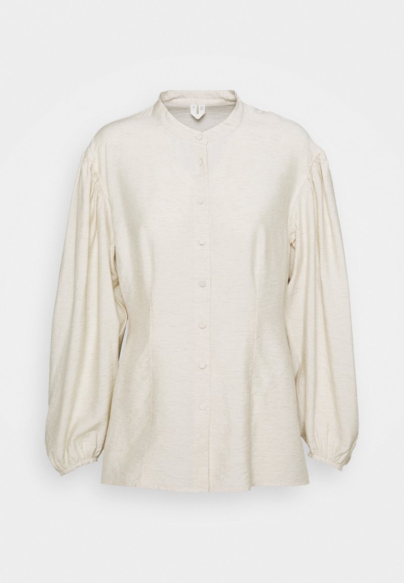 Blouse longue manches longues blanc cassé avec col rond, devant boutonné et manches bouffantes froncées avec poignets élastiques.