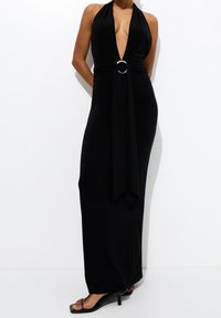 Robe maxi noire à col licou avec un décolleté en V profond, taille cintrée ornée d'une bague argentée, et jupe fluide. Tissu lisse sans motifs.