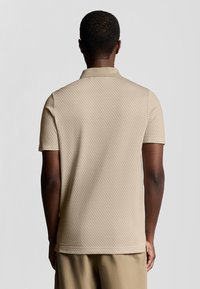 Beige Poloshirt mit kurzen �Ärmeln, einem strukturierten Muster und einem klassischen Kragen. Das Design bietet einen geraden Saum und seitliche Schlitze für zusätzlichen Komfort.