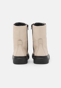 Botines de cuero beige con textura suave, cierres laterales de cremallera negra y suela de goma negra gruesa.