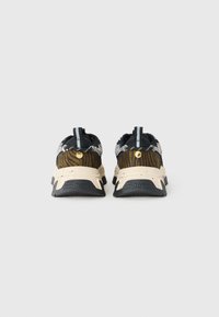 Par de zapatillas de animal print en negro y marrón con suelas moteadas en beige, vistas desde atrás sobre un fondo blanco.