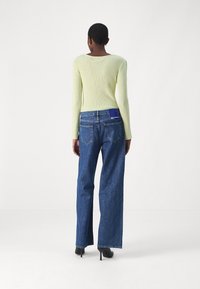 Světle žlutý žebrovaný top s dlouhým rukávem v kombinaci s modrými širokými džínami. Džíny mají zadní kapsu a kontrastní modrou nášivku. Boty na podpatku.