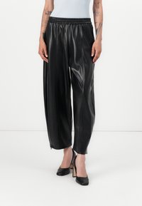 Zwarte faux leren broeken met een elastische tailleband, wijde pijpen, voornaad en ritsen bij de enkels, gecombineerd met zwarte hoge hakken.