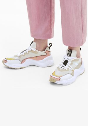 Des baskets Puma arborant un schéma de couleurs blanc, beige et rose, avec une tige texturée, des coutures contrastantes et une semelle épaisse avec une adhérence en caoutchouc.